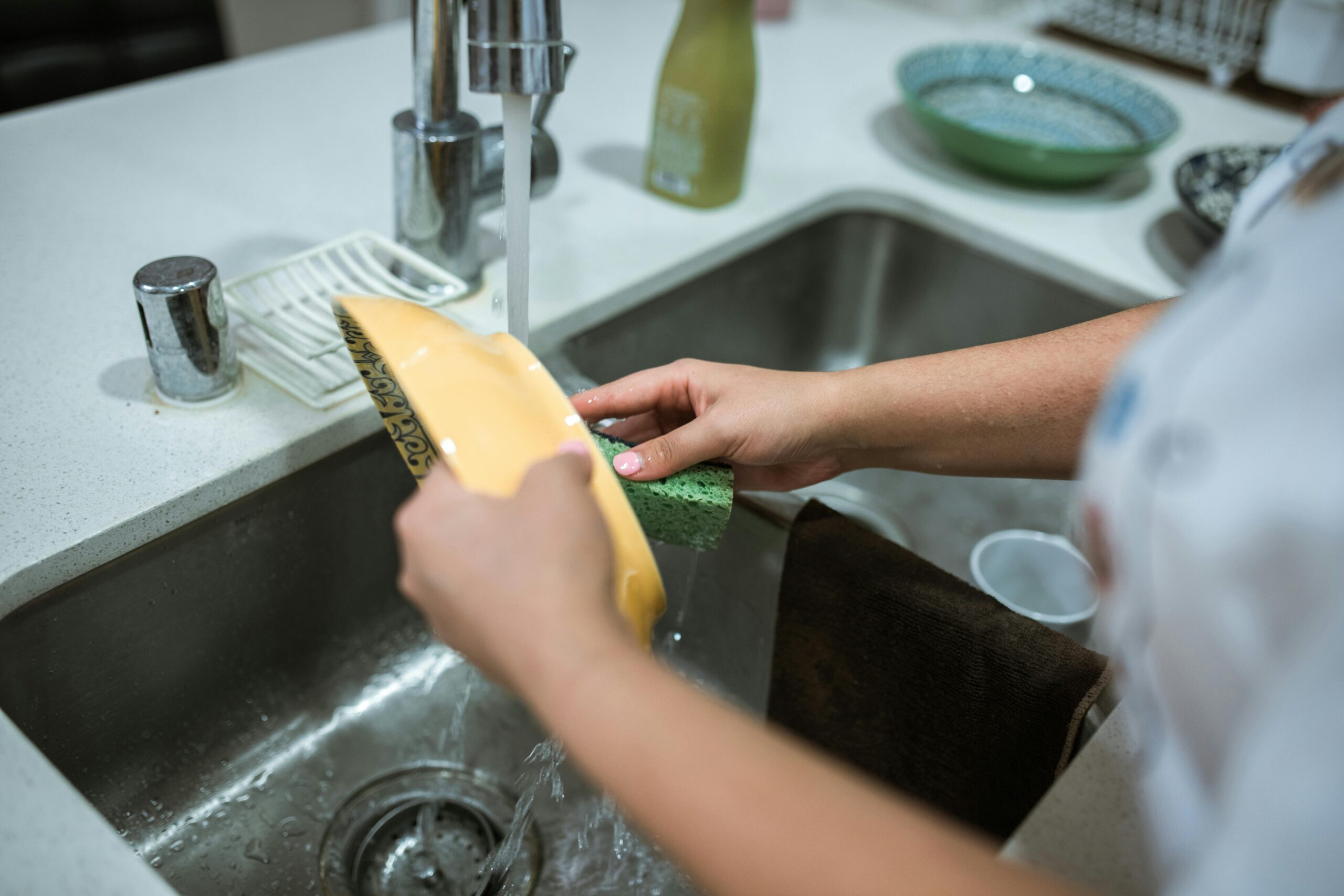 Close-up of hands washing dishes in a kitchen sink with running water.